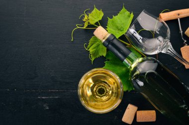 Bir şişe beyaz şarap gözlük ve üzüm. Üzüm yaprakları. Üstten görünüm. Siyah ahşap arka plan üzerinde. Metin için boş alan.
