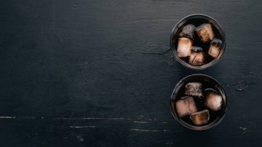Bir bardak buzlu viski. Rom-kola. Brandy. Siyah ahşap arka plan üzerinde. Üstten görünüm. Metin için boş alan.