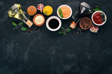 Soslar - ketçap, mayonez, hardal, soya sosu, Barbekü sos, biber ve baharat ayarlayın. Siyah taş arka plan üzerinde. Üstten görünüm. Metin için boş alan.