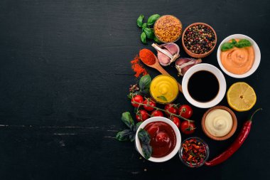 Soslar siyah bir ahşap arka plan ayarla. Ketçap, mayonez, hardal, soya sosu, Barbekü sos, biber ve baharat. Üstten görünüm. Metin için boş alan.