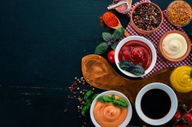 Soslar siyah bir ahşap arka plan ayarla. Ketçap, mayonez, hardal, soya sosu, Barbekü sos, biber ve baharat. Üstten görünüm. Metin için boş alan.