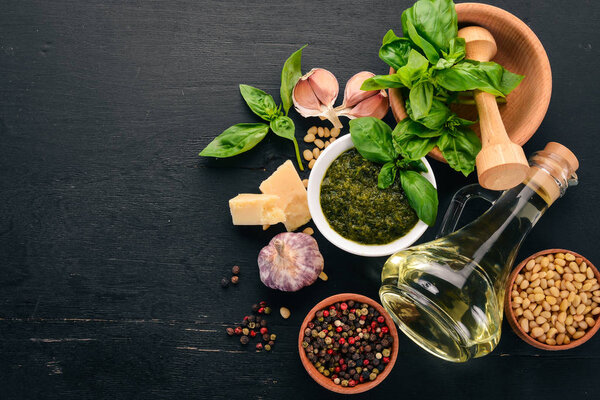 Preparing basil pesto sauce. Basil, parmesan cheese, olive oil. Top view. On a black wooden background. Free space for text.