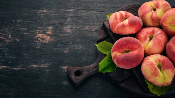 Düz şeftali yeşil siyah bir ahşap arka plan üzerinde bırakır. Üstten görünüm. Metniniz için boş alan.