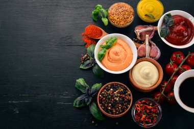 Soslar siyah bir ahşap arka plan ayarla. Ketçap, mayonez, hardal, soya sosu, Barbekü sos, biber ve baharat. Üstten görünüm. Metin için boş alan.