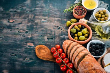Zeytin, zeytinyağı, ekmek, peynir ve baharat kümesi. Siyah ahşap arka plan üzerinde. Metin için boş alan.