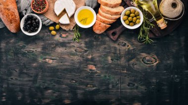 A set of olives, olive oil, bread, cheese and spices. On a black wooden background. Free space for text. clipart