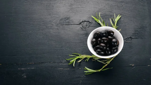 Olives in a plate and rosemary. On a black wooden background. Free space for text.