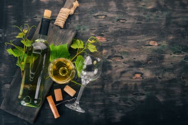 Bir şişe beyaz şarap gözlük ve üzüm. Üzüm yaprakları. Üstten görünüm. Siyah ahşap arka plan üzerinde. Metin için boş alan.
