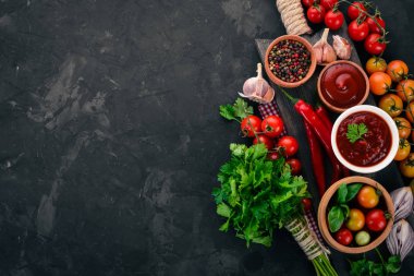 Bir kase içinde ketçap sosu. Kiraz domates, baharat, biber, zeytin yağı, maydanoz. Üstten görünüm. Taş bir arka plan üzerinde. Metin için boş alan.