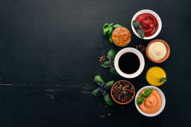 Set the sauces on a black wooden background. Ketchup, mayonnaise, mustard, soy sauce, barbecue sauce, pepper and spices. Top view. Free space for text. clipart