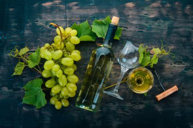 Bir şişe beyaz şarap gözlük ve üzüm. Üzüm yaprakları. Üstten görünüm. Siyah ahşap arka plan üzerinde. Metin için boş alan.