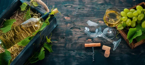 A bottle of white wine with glasses and grapes. Leaves of grapes. Top view. On a black wooden background. Free space for text.