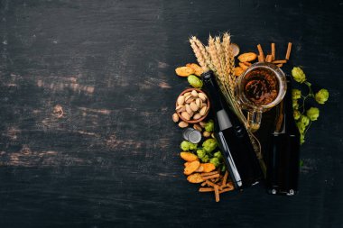 Bira ve aperatifler. Tuzlu kraker, kurutulmuş balık, cips, fındık, fıstık, fıstık. Siyah ahşap arka plan üzerinde. Metin için özgür yer. Üstten görünüm.