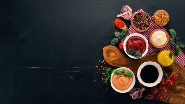Soslar siyah bir ahşap arka plan ayarla. Ketçap, mayonez, hardal, soya sosu, Barbekü sos, biber ve baharat. Üstten görünüm. Metin için boş alan.