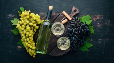 Bir cam ve üzüm ile bir şişe beyaz şarap. Siyah ahşap arka plan üzerinde. Metin için özgür yer. Üstten görünüm.