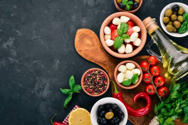 Bir caprese salatası yemek. Mozzarella peyniri, domates, zeytin, fesleğen yaprağı, yağ, karabiber. Siyah taş masanın üstünde. Metin için boş alan.