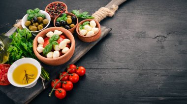 İtalyan caprese salatası için malzemeler. Mozzarella peyniri, kiraz domates, fesleğen yaprağı, zeytin, yağ, karabiber. Siyah ahşap arka plan üzerinde. Metin için boş alan.