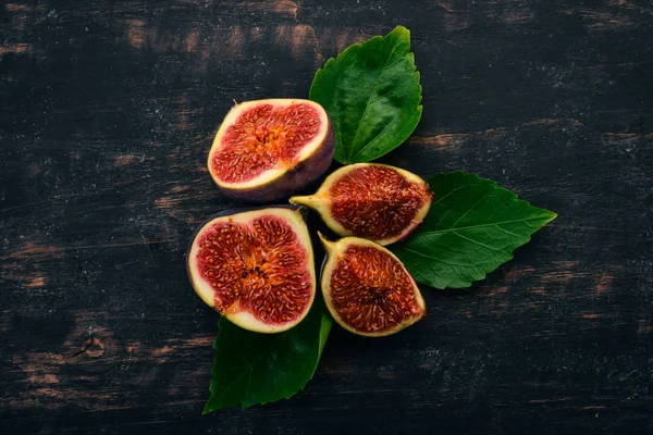 Fresh figs with leaves on a black wooden table. Free space for text. Top view.