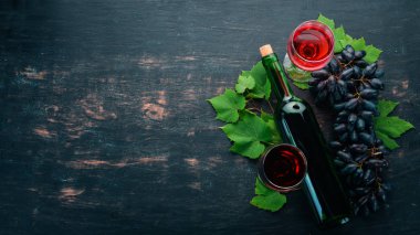 Bir cam ve üzüm ile bir şişe kırmızı şarap. Siyah ahşap arka plan üzerinde. Metin için özgür yer. Üstten görünüm.