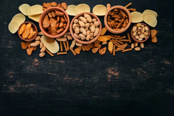 Snack for beer. Salted crackers, chips, nuts, peanuts, pistachios. On a wooden background. Free space for text. Top view.