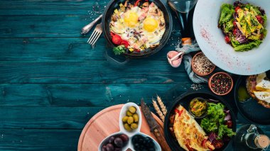 Bir dizi yemek. Shakshuka, omlet, avokado salata, haşlanmış yumurta ile sandviç. Ahşap bir arka plan üzerinde. Metin için özgür yer. Üstten görünüm.