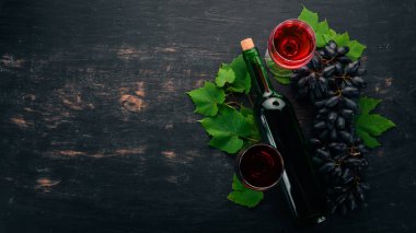Bir cam ve üzüm ile bir şişe kırmızı şarap. Siyah ahşap arka plan üzerinde. Metin için özgür yer. Üstten görünüm.