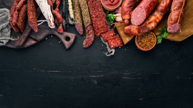 Salam ve aperatifler ürün yelpazesine. Sosis Amandine, sosis, salam, paperoni. Siyah ahşap arka plan üzerinde. Üstten görünüm. Metniniz için boş alan.