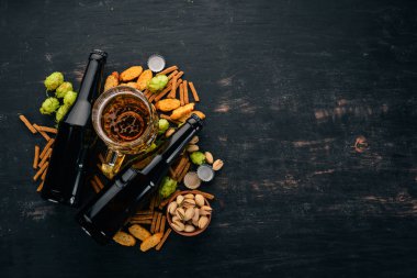 Bira ve aperatifler. Tuzlu kraker, kurutulmuş balık, cips, fındık, fıstık, fıstık. Siyah ahşap arka plan üzerinde. Metin için özgür yer. Üstten görünüm.