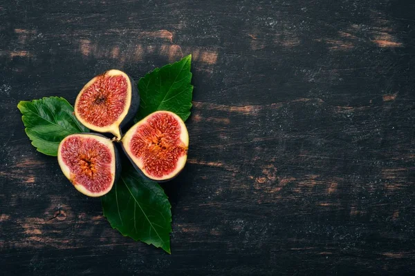 Fresh figs with leaves on a black wooden table. Free space for text. Top view.