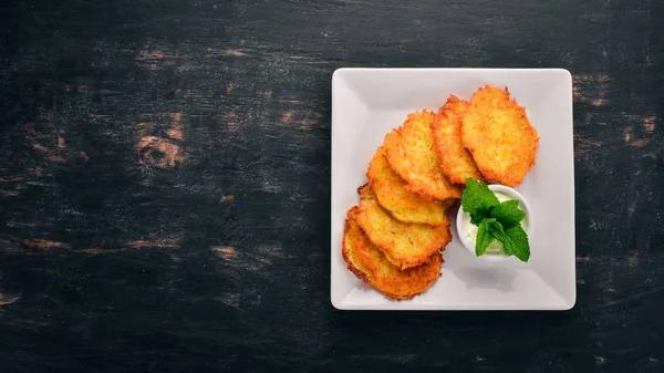 Potato cakes with sour cream. Potato pancakes. Ukrainian cuisine. On the old wooden background. Free space for text. Top view.