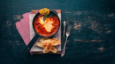 Domates ve bir tavada tost ekmeği ile yumurta. Shakshuka üst görünümü. Metniniz için boş alan. Ahşap bir arka plan üzerinde.