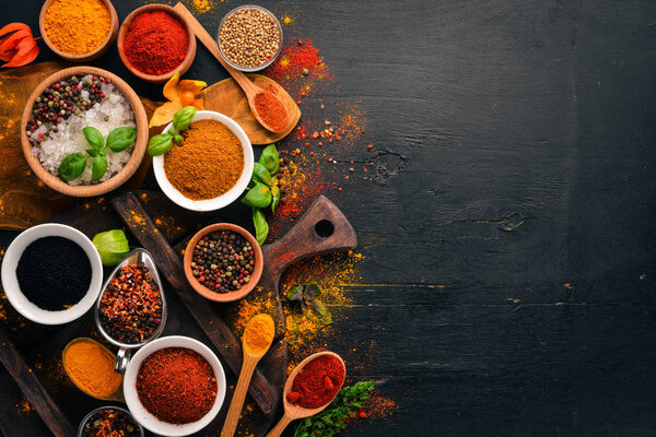 Spices and herbs on a wooden board. Pepper, salt, paprika, basil, turmeric. On a black wooden chalkboard. Top view. Free copy space.