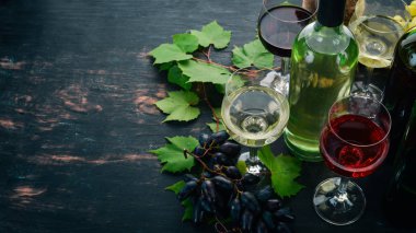 Kırmızı ve beyaz şarap şişeleri ve gözlük kümesi. Üzüm. Siyah ahşap arka plan üzerinde. Metin için özgür yer. Üstten görünüm.