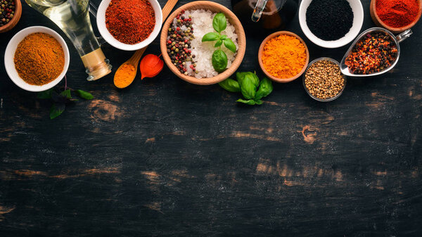 A set of spices and herbs. Indian cuisine. Pepper, salt, paprika, basil, turmeric. On a black wooden chalkboard. Top view. Free copy space.