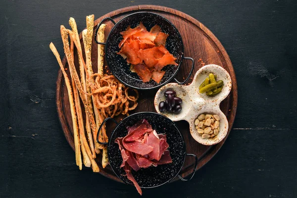 A selection of snacks for beer. Fish, prosciutto, peanuts, olives. On a wooden background. Free copy space. Top view.