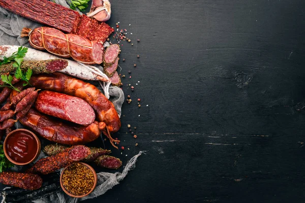 Salam ve aperatifler ürün yelpazesine. Sosis Amandine, sosis, salam, paperoni. Siyah ahşap arka plan üzerinde. Üstten görünüm. Metniniz için boş alan.