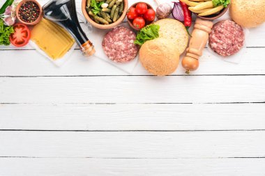 Burger hazırlanması. Eti, domates, soğan. Beyaz ahşap zemin üzerinde. Üstten görünüm. Ücretsiz kopya alanı.