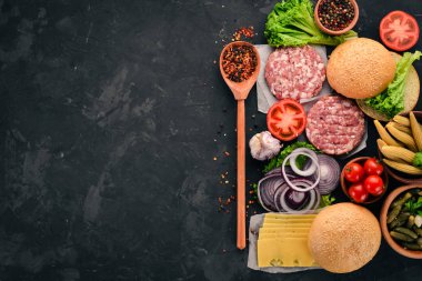 Burger hazırlanması. Eti, domates, soğan. Siyah taş arka plan üzerinde. Üstten görünüm. Ücretsiz kopya alanı.