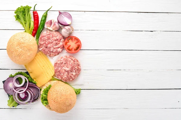 Preparation of burger. Meat, tomatoes, onions. On a white wooden background. Top view. Free copy space.