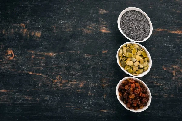 Raisins, sunflower seeds and poppy seeds. On a black wooden background. Top view. Free copy space.