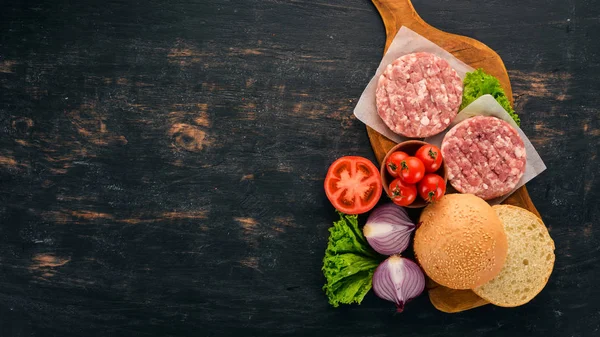 Raw burger Cooking a burger with meat. On a black wooden background. Top view. Free copy space.