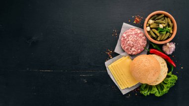 Burger hazırlanması. Et, taze sebze, domates, soğan. Siyah ahşap arka plan üzerinde. Üstten görünüm. Ücretsiz kopya alanı.