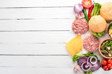Burger hazırlanması. Eti, domates, soğan. Beyaz ahşap zemin üzerinde. Üstten görünüm. Ücretsiz kopya alanı.