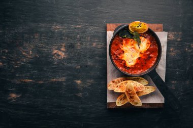 Domates ve bir tavada tost ekmeği ile yumurta. Shakshuka üst görünümü. Metniniz için boş alan. Ahşap bir arka plan üzerinde.