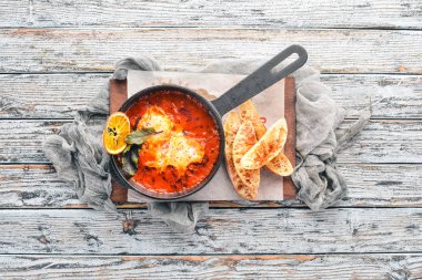 Domates ve bir tavada tost ekmeği ile yumurta. Shakshuka üst görünümü. Metniniz için boş alan. Ahşap bir arka plan üzerinde.