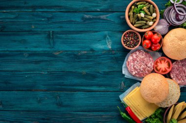 Burger hazırlanması. Eti, domates, soğan. Mavi ahşap arka plan üzerinde. Üstten görünüm. Ücretsiz kopya alanı.