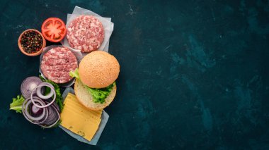 Burger hazırlanması. Eti, domates, soğan. Siyah taş arka plan üzerinde. Üstten görünüm. Ücretsiz kopya alanı.