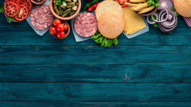 Burger hazırlanması. Eti, domates, soğan. Mavi ahşap arka plan üzerinde. Üstten görünüm. Ücretsiz kopya alanı.