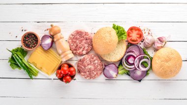Burger hazırlanması. Eti, domates, soğan. Beyaz ahşap zemin üzerinde. Üstten görünüm. Ücretsiz kopya alanı.