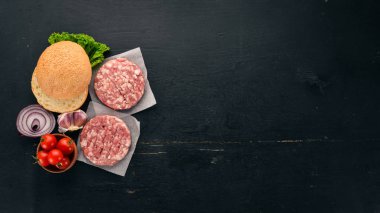 Burger hazırlanması. Et, taze sebze, domates, soğan. Siyah ahşap arka plan üzerinde. Üstten görünüm. Ücretsiz kopya alanı.